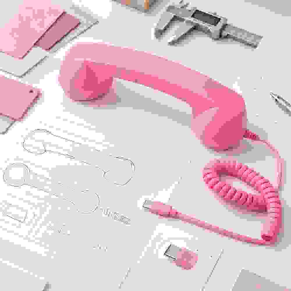 Pink retro phone handset with USB Type-C cable, technical drawing, color swatches and measuring tools on a product development workspace Pink retro phone handset with USB Type-C cable, technical drawing, color swatches and measuring tools on a product development workspace