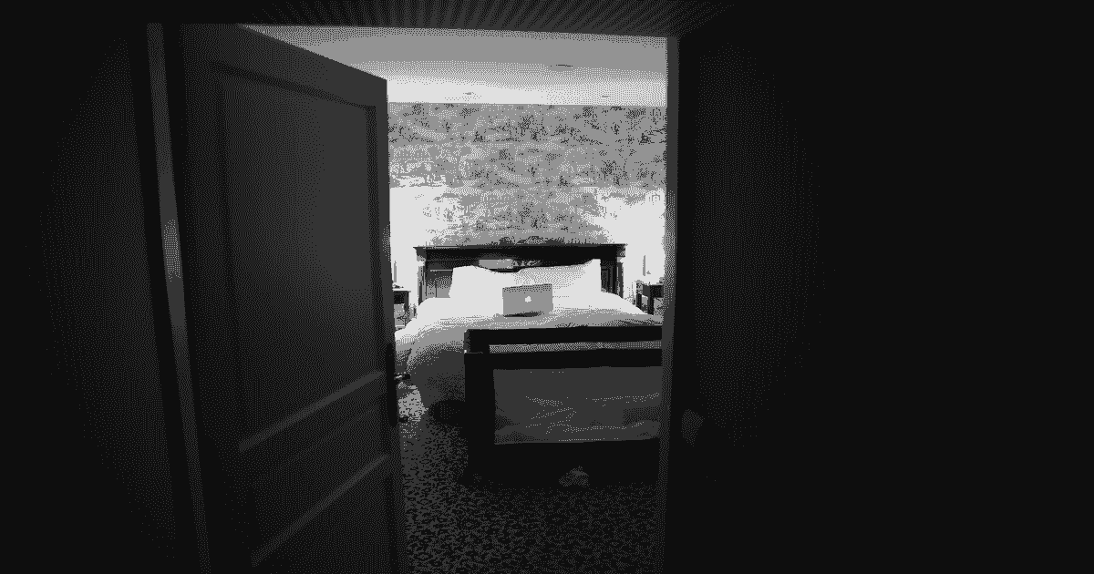 Bedroom door open with MacBook sitting on top of bed with white bed sheets in black and white.