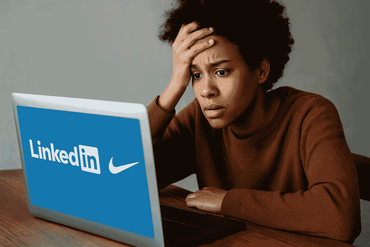 **Alt text:** An androgynous person with medium brown skin sits at a wooden desk, looking worriedly at a laptop screen displaying the LinkedIn and Nike logos. They rest one hand on their forehead, realising they may have been scammed, in a softly lit modern home setting.