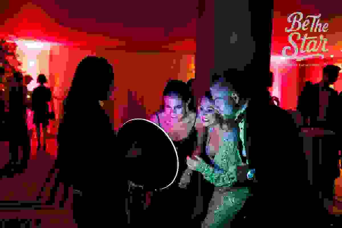 Event guests viewing their photo as an attendant uses a roaming photo booth during a corporate or wedding event. Event guests viewing their photo as an attendant uses a roaming photo booth during a corporate or wedding event.