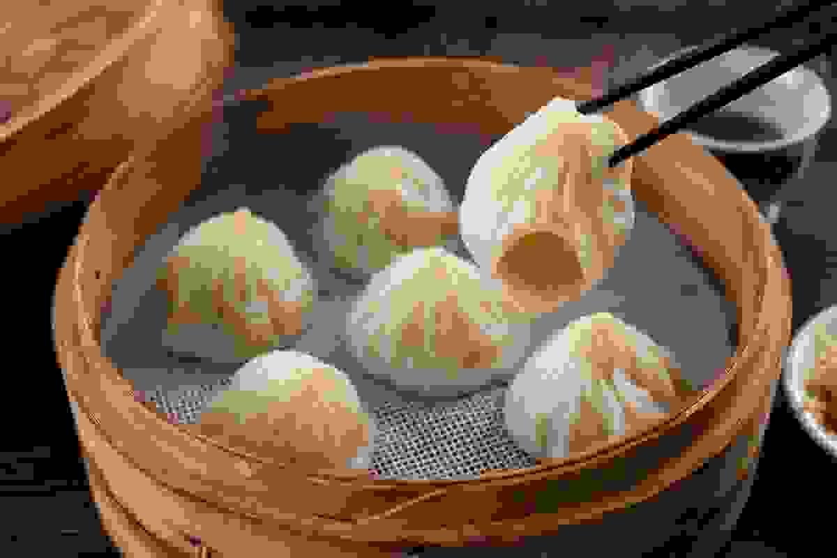 Stacked bamboo steamers of xiao long bao in a bustling dim sum kitchen, steam rising from the freshly opened lid. Stacked bamboo steamers of xiao long bao in a bustling dim sum kitchen, steam rising from the freshly opened lid.