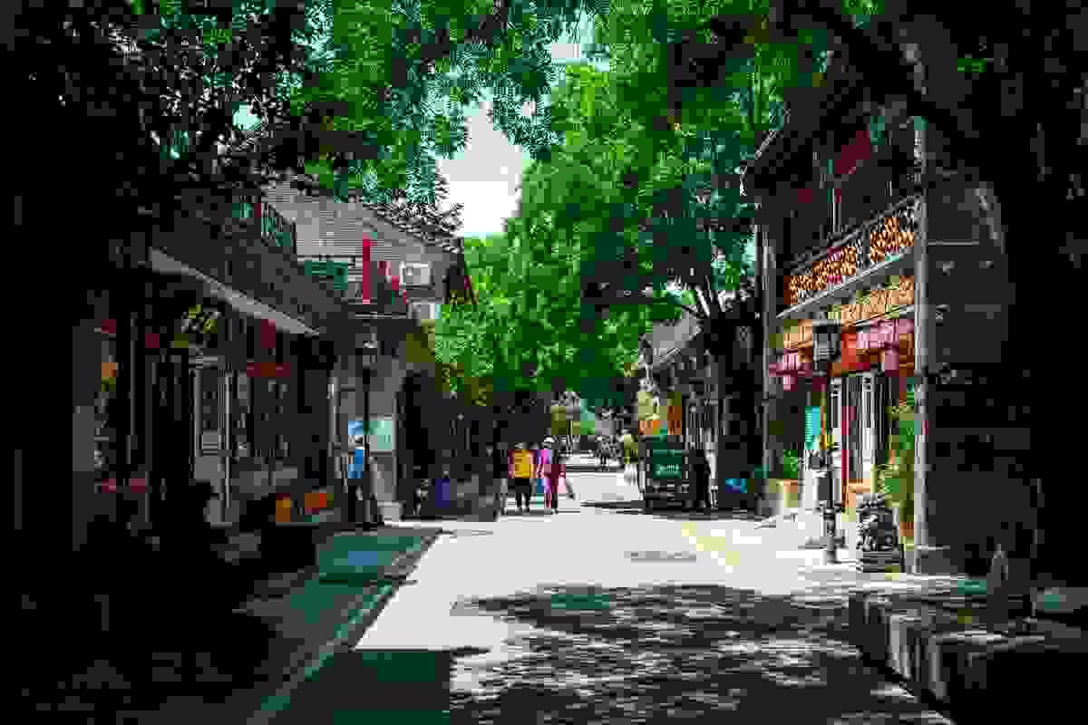 A traditional Beijing hutong alley with bicycles, a scooter, and vibrant red lanterns hanging overhead A traditional Beijing hutong alley with bicycles, a scooter, and vibrant red lanterns hanging overhead