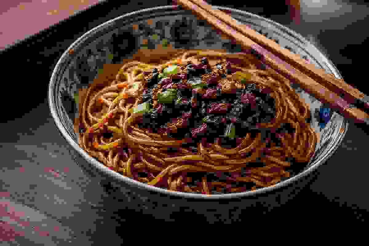 Shanghai scallion oil noodles in a ceramic bowl, glossy noodles coated in dark soy sauce and fragrant scallion oil, topped with crispy fried scallions, chopsticks resting on the bowl, dark wood tabletop. Shanghai scallion oil noodles in a ceramic bowl, glossy noodles coated in dark soy sauce and fragrant scallion oil, topped with crispy fried scallions, chopsticks resting on the bowl, dark wood tabletop.