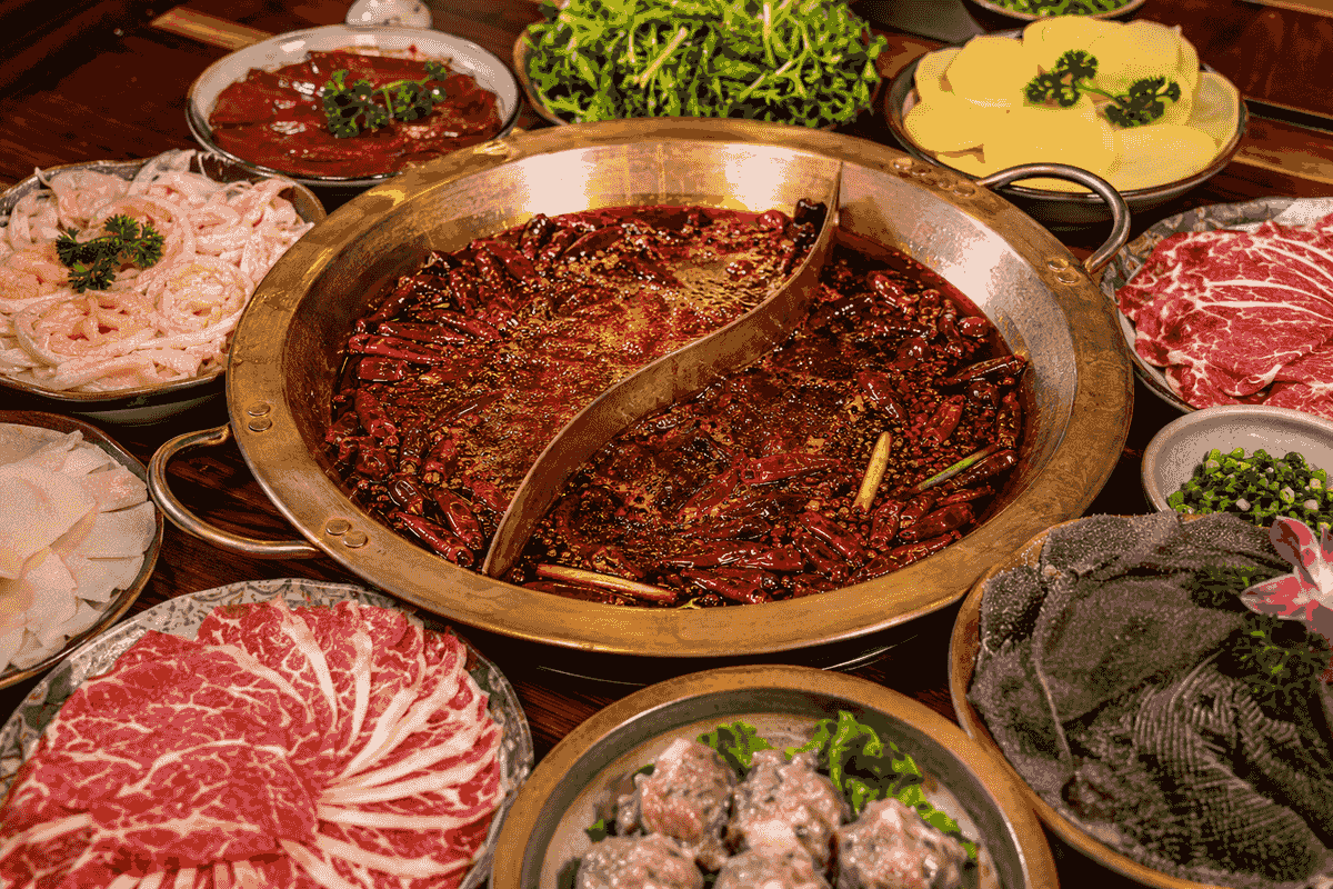 Spicy Chongqing hot pot with red chili broth and fresh ingredients on a restaurant table Spicy Chongqing hot pot with red chili broth and fresh ingredients on a restaurant table