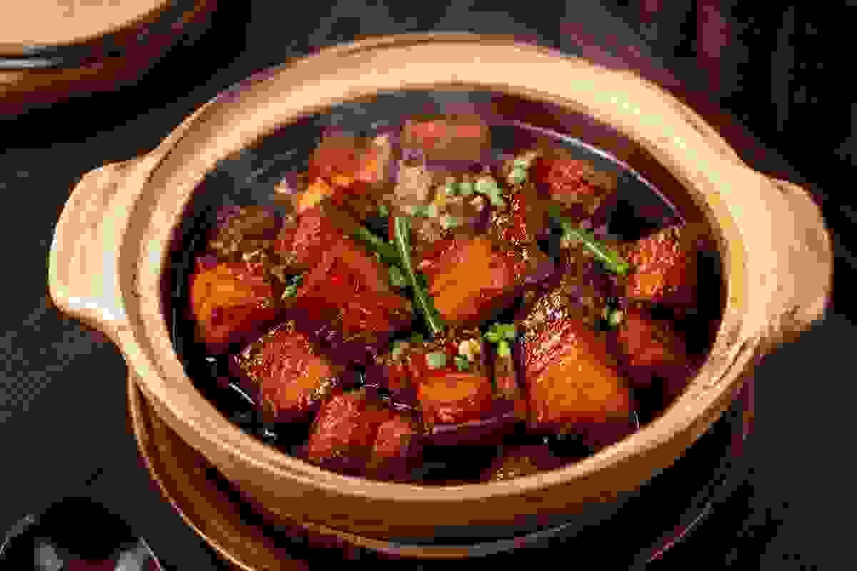 hanghai-style braised pork belly in a traditional clay pot, tender glossy chunks of pork simmered in rich dark soy-based caramelized sauce, garnished with green onion, warm indoor lighting. hanghai-style braised pork belly in a traditional clay pot, tender glossy chunks of pork simmered in rich dark soy-based caramelized sauce, garnished with green onion, warm indoor lighting.