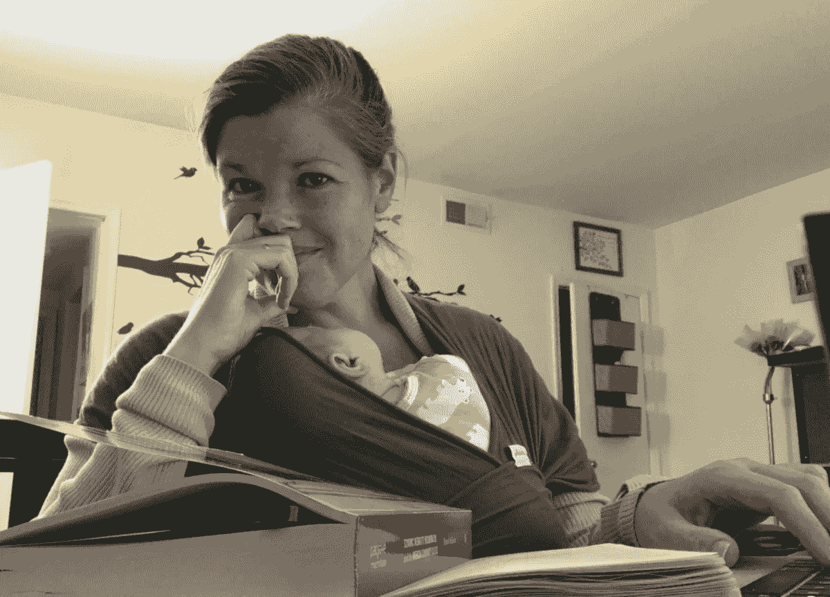 Robyn holding a baby while typing with books open Robyn holding a baby while typing with books open