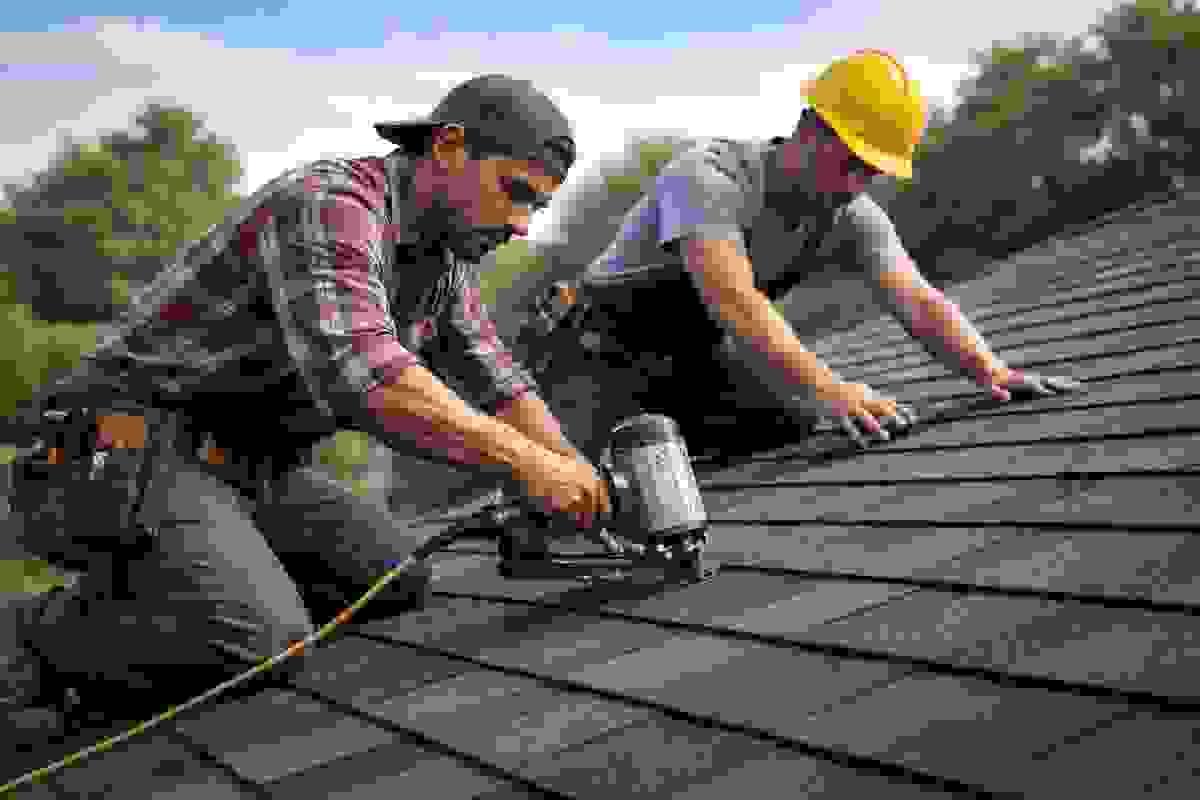 Two roofing contractors installing new asphalt shingles during a full roof replacement in Austin, Texas Two roofing contractors installing new asphalt shingles during a full roof replacement in Austin, Texas