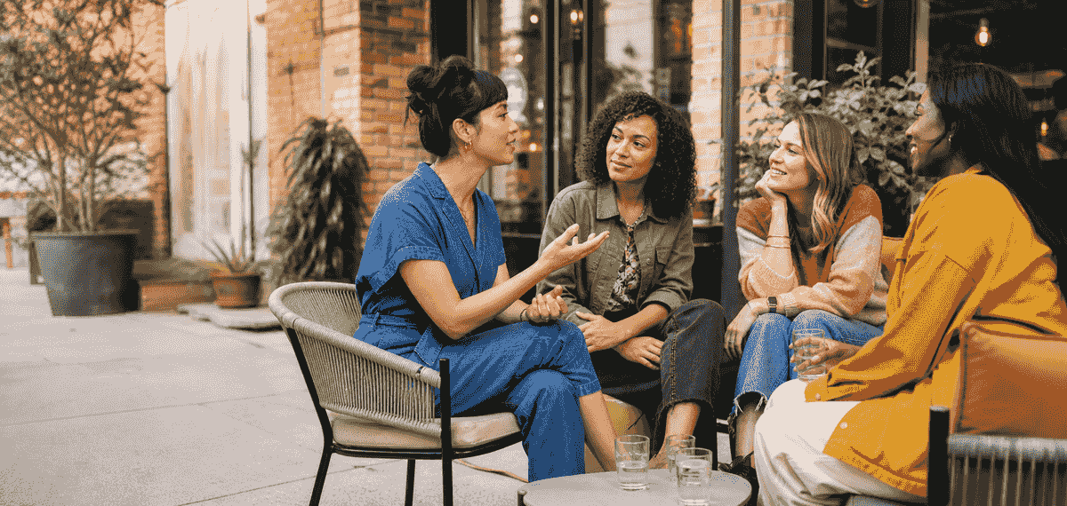 Four diverse women seated together in a lively, thoughtful conversation at a neighborhood café. Four diverse women seated together in a lively, thoughtful conversation at a neighborhood café.