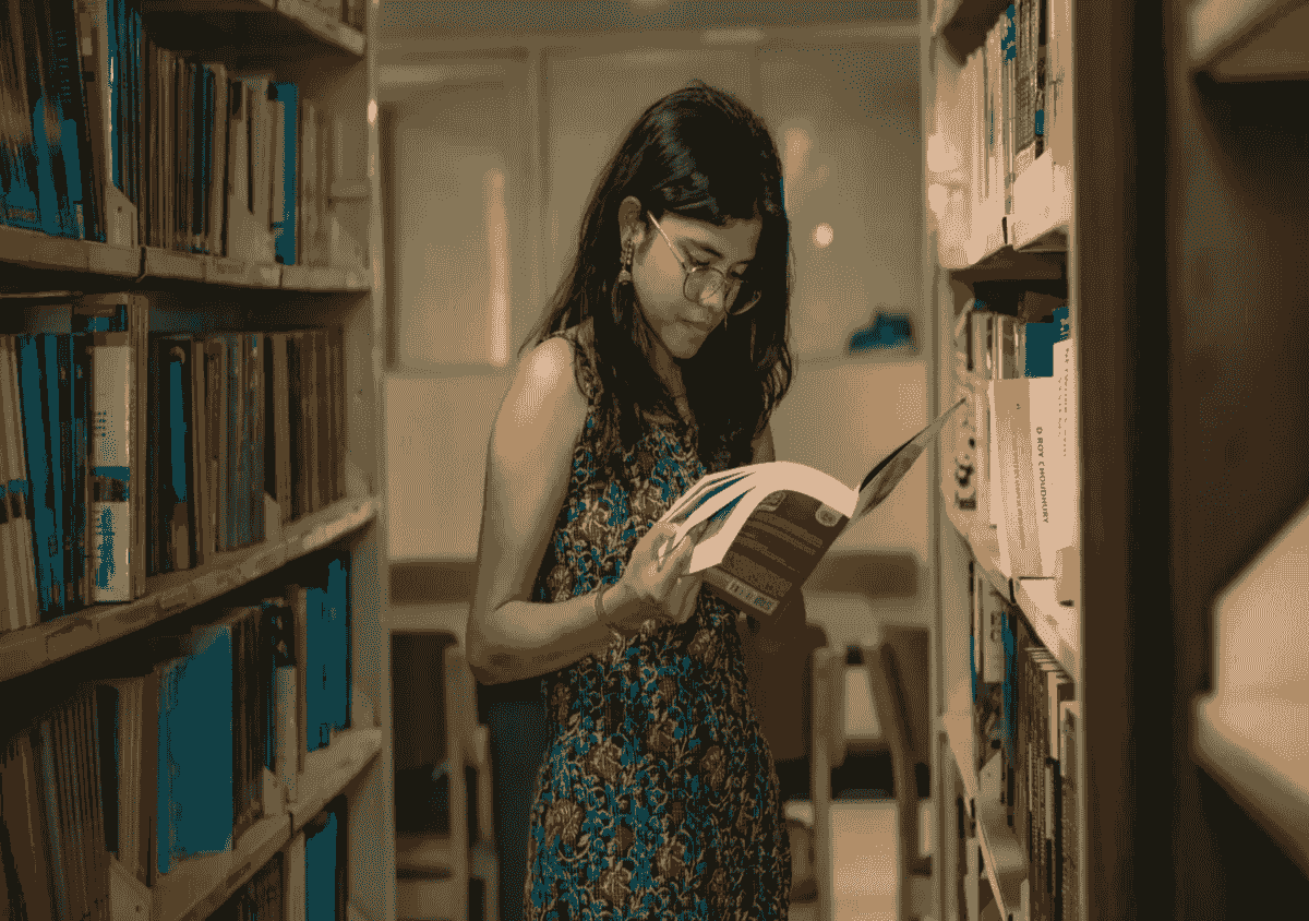 Oriental female wearing glasses and flower-patterned dress while standing in a library aisle reading a book. Oriental female wearing glasses and flower-patterned dress while standing in a library aisle reading a book.