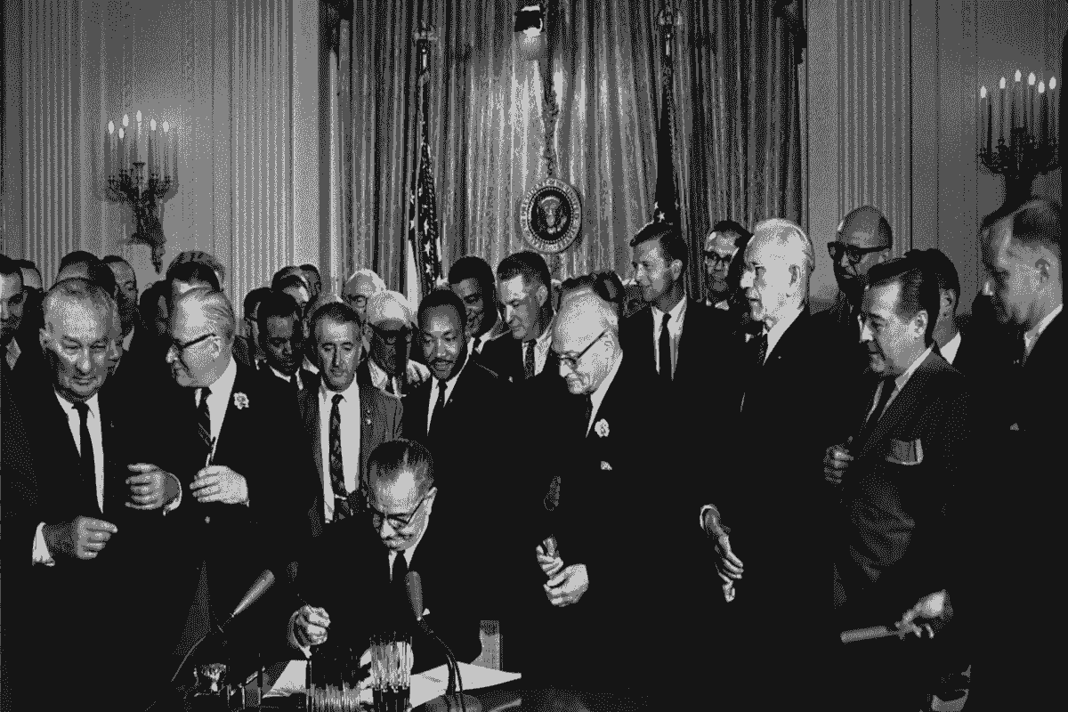 Black and white photo of a group of men and women standing or sitting in front of a building. Black and white photo of a group of men and women standing or sitting in front of a building.