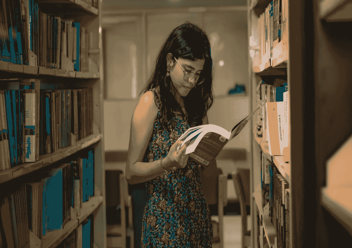 Oriental female wearing glasses and flower-patterned dress while standing in a library aisle reading a book. Oriental female wearing glasses and flower-patterned dress while standing in a library aisle reading a book.