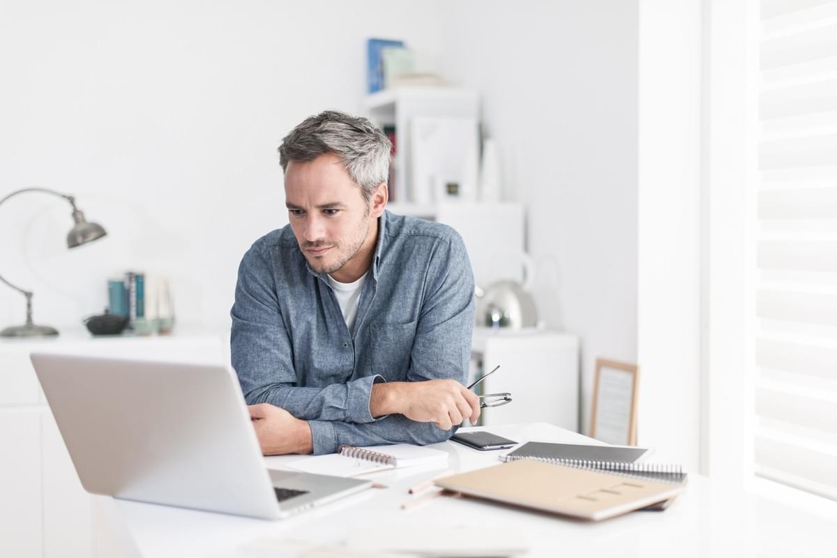Middle Aged Man Sitting at Desk Researching Neurology Compounded Medications on Laptop 