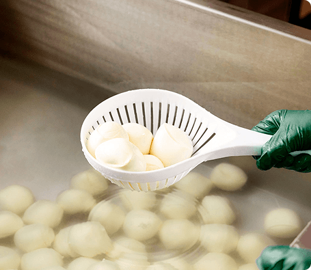 Mozzarella balls being lifted from natural brine during production.