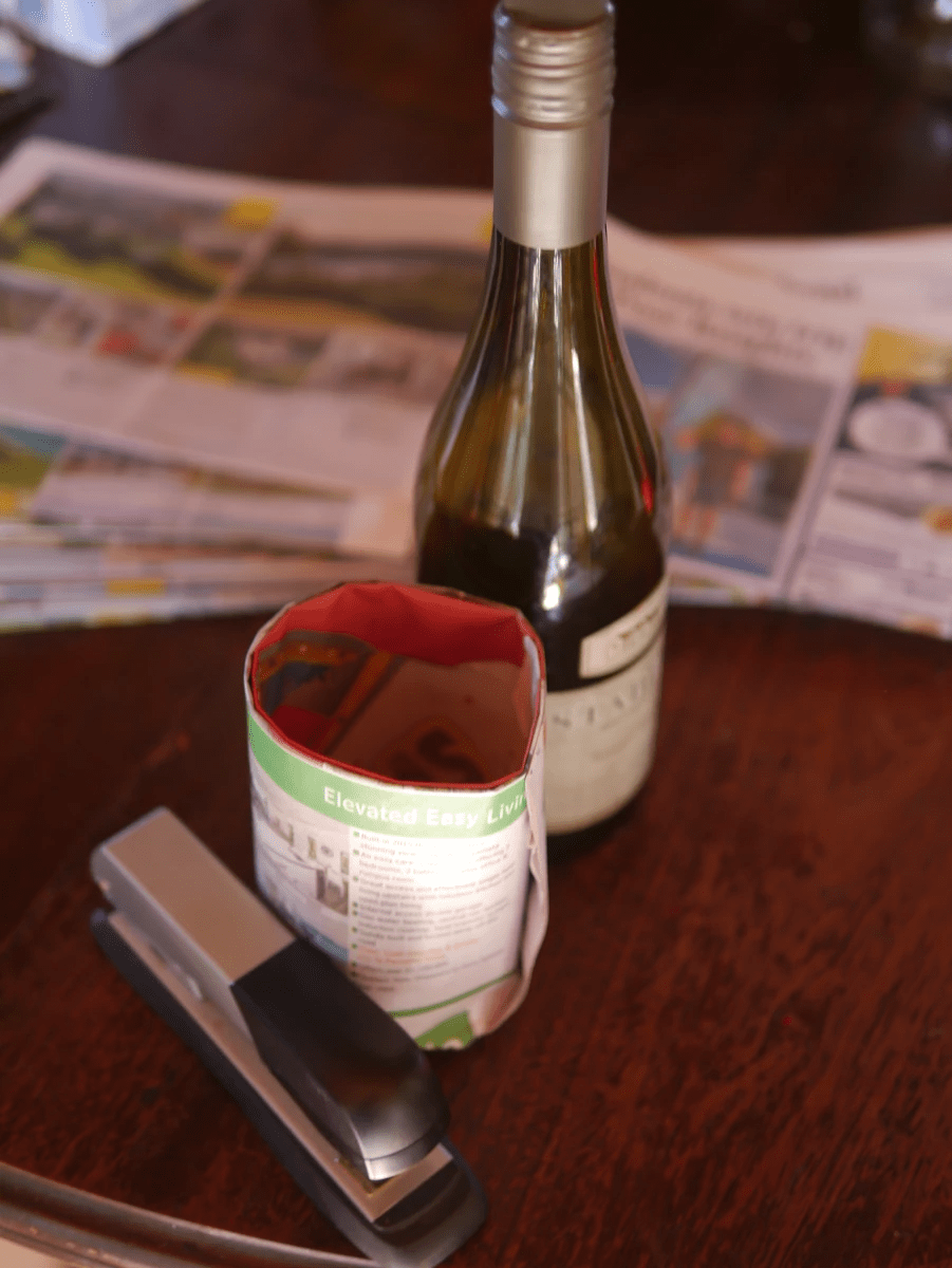 Rolling biodegradable seedling pots using newspaper, a wine bottle as a mold, and a stapler - a sustainable alternative to plastic pots.