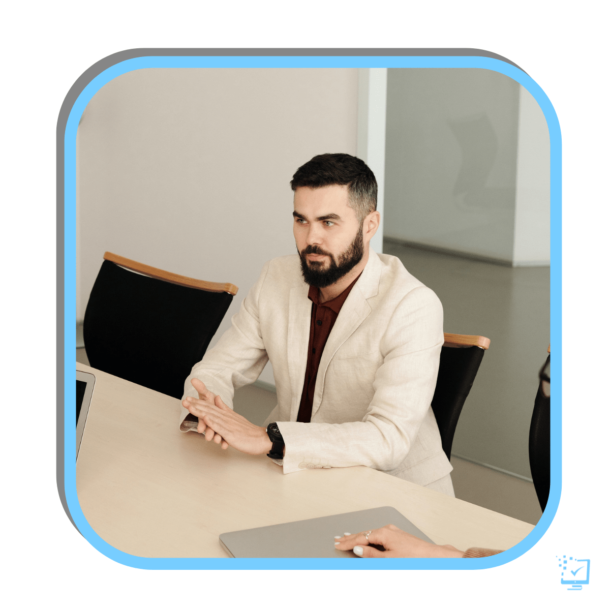 A young man is sitting at a work table with two other people sitting across from him. The young man has a serious face.