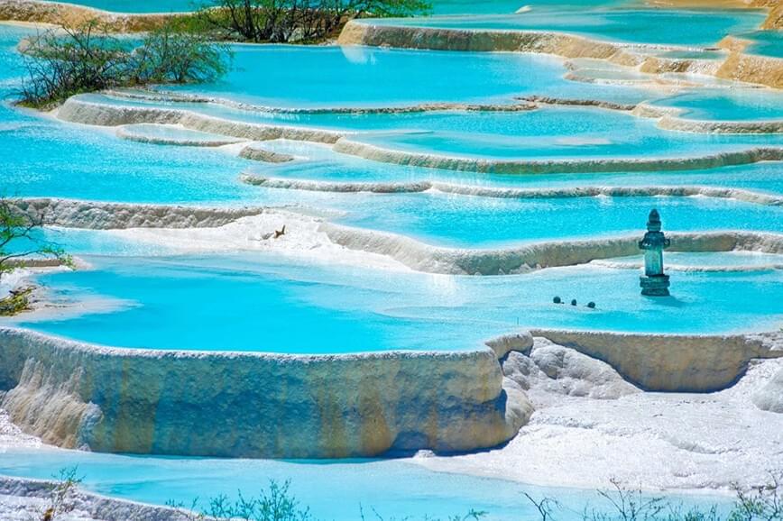 1992年にユネスコにより世界自然遺産に指定された四川省の景勝地。 岷山山脈の主峰・標高5,588mの雪宝頂の麓に連続してできた棚田状の3400もの湖沼群を清水が流れ落ちる様が黄金の龍に見えることから「黄龍」と呼ばれます。長さ約3.6km、標高差約400m。2006年にロープウェイが設置され、上りの続く黄龍寺近くまでロープウェイで昇ることができます。風景区内の見所は「迎賓池」、「盆景池」、「五彩池」などと名付けられ、それぞれの見所を結ぶ遊歩道が整備されています。景観の他にも、黄龍寺には黄龍の神様、黄龍真人が祀られ地元の人々の信仰を集めています。また、頂上の五彩池は場所と時間によって緑、黄、青、白など水面の色を変えることで有名です。