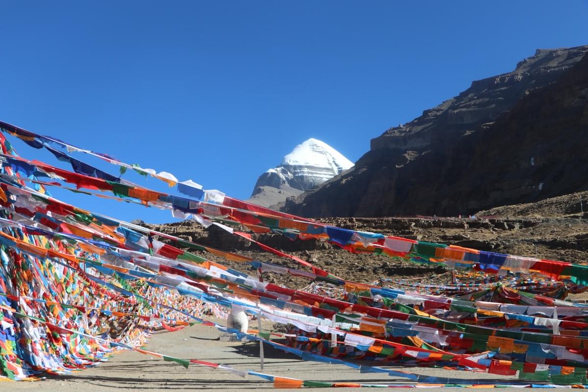 カン・リンポチェ聖山ブログ｜転山完全ガイド＋グゲ王朝・東嘎皮央遺跡解説＋道中絶景  チベット・アリ地方——「世界の屋根の屋根」と呼ばれるこの地に、カン・リンポチェ（岡仁波斉、標高6,656m） は静かに屹立しています。 チベット仏教・ボン教・ヒンドゥー教・ジャイナ教、四大宗教すべてから「世界の中心」と崇められる聖山。 ピラミッドのように整った山容、万年雪に覆われた頂、朝陽に金く染まる姿——その神々しさは、言葉では表現しきれません。 この旅では、カン・リンポチェ転山（聖山一周トレッキング） の詳細、道中の絶景、そしてアリ地方に残るグゲ王朝遺跡・東嘎皮央石窟の謎と美しさを、たっぷりとお届けします。 一、カン・リンポチェとは？｜世界の中心に佇む聖山  カン・リンポチェは岡底斯山脈の主峰で、アリ地方プラン県に位置します。 周囲にはヒマラヤ山脈・カラコルム山脈・崑崙山脈が連なり、「雪山に囲まれた聖地」と呼ばれます。 また、四大聖河の源でもあります。  • 獅子泉河（インダス川へ）  • 孔雀河（ガンジス川へ）  • 馬泉河（ヤルツァンポ川へ）  • 象泉河（サトレジ川へ）  古くから「この山を一周すれば、一年の罪が浄化される」と信じられ、今も世界中から巡礼者が絶えません。 二、カン・リンポチェ転山（聖山一周）完全解説  「転山（ジョンシャン）」とは、カン・リンポチェの麓を時計回りに一周する巡礼トレッキングのことです。 信仰を込めて歩く伝統的な行程で、現在は世界中のトレッカーに人気です。  1. 基本情報  • 総距離：約52km  • 標準日程：2泊3日（初心者向け）  • 最高標高：ドルマラ峠（約5,630m）  • 必須ルール：必ず時計回り（宗教的慣習のため、逆回りは厳禁）  2. 日程別ルートと道中の景色  1日目：スタート地点（タルチェン）→チョクグ寺周辺（宿泊）  • 標高：4,700m前後  • 道のり：なだらかな高原道、草原と砂利道が中心  • 見どころ：  ◦ 遠くにカン・リンポチェの雄姿を望む  ◦ マニ石（祈りの石）や経幡（風の祈り旗）が道端に連なる  ◦ 青空と草原、時折ヤクや羊の群れが現れる高原の風景  2日目：チョクグ寺→ドルマラ峠→中間宿泊地（最も過酷な日）  • 標高差：5,000m→5,630m→5,000m  • 道のり：坂道が続き、高地特有の息切れを感じやすい  • 見どころ：  ◦ 峠手前：荒涼とした岩場と氷河の痕跡  ◦ ドルマラ峠：カン・リンポチェを真横から望む絶景ポイント、雪嶺が眼前に迫る  ◦ 峠越え後：広大な荒原と遠くの山々が連なる、圧倒的なスケール感  3日目：宿泊地→スタート地点（完走）  • 道のり：下り中心、足取りが軽くなる  • 見どころ：  ◦ 朝の光に照らされるカン・リンポチェの山肌  ◦ 小川や湿地、高原の花（季節による）  ◦ ゴール地点での達成感と、聖山からの「浄化」を実感  3. 転山の心構え  高地のため速く歩くのは厳禁。 「ゆっくり、ゆっくり」を合言葉に、呼吸を整えながら一歩ずつ進めてください。 道中は巡礼者同士が互いに励まし合う、温かい雰囲気があります。 三、アリ地方の至宝｜グゲ王朝遺跡と東嘎皮央石窟  カン・リンポチェを後にし、車で西へ約250km——札達（ザンダ）県に入ると、眼前には土林（トゥーリン） と呼ばれる奇観が広がります。 億万年の風雨が削り上げた粘土の柱々が、まるで「大地の彫刻庭園」のように連なります。 この土林の中に、700年にわたりアリ地方を支配し、忽然と消えた謎の王朝——グゲ王朝 の遺跡が眠っています。  1. グゲ王朝遺跡（ツァパラン城址）  • 時代：10世紀～17世紀（チベット帝国崩壊後、吐蕃王族が建国）  • 場所：札達県象泉河畔、標高3,800mの土林の丘上  • 特徴：  ◦ 全高115m、300mに及ぶ巨大な土造りの城郭  ◦ 王宮・寺院・住宅が階層的に配置された「立体都市」  ◦ 城内には1,000年前の美しい壁画が残り、仏教画や王族の生活が描かれています  • 謎：17世紀、一夜にして住民が姿を消し、廃城となった理由は今も不明。  朝陽が城壁を黄金色に染める瞬間は、まさに「時空を超えた美しさ」です。  2. 東嘎皮央（トンガ・ピヤン）石窟遺跡  グゲ王朝の副都・文化センターとして栄えたのが、東嘎村・皮央村にまたがる石窟群です。 「チベットの敦煌」とも呼ばれ、中国最大級の仏教石窟遺跡として知られています。  • 時代：古格王朝最盛期（10～11世紀）  • 構成：寺院・城郭・千を超える石窟・塔林から成る  • 最大の見どころ：鮮やかに残る壁画  ◦ 仏伝物語、菩薩、飛天、孔雀・象などの動物が描かれ  ◦ インド・西域・中央アジアの様式が融合した、国際色豊かな美しさ  ◦ 暗い石窟の中に灯りをともすと、1,000年前の色彩が今に蘇る  土林の丘に無数の洞窟が開いた光景は、まるで「蜂の巣城」のようで、神秘的な雰囲気に包まれます。 四、カン・リンポチェ＆アリ旅行 必守注意事項  1. 高山病対策（最優先）  アリ地方は平均標高4,500m超、高山病リスクが極めて高いです。  • チベット到着後、1～2日は絶対に休養、無理な運動禁止  • アルコール・喫煙は厳禁  • 水分を1日2～3L摂取（脱水が高山病を悪化させる）  • 頭痛・吐き気・息切れが出たら即休憩・下山、薬を事前に準備  2. 服装・装備（天気が急変！）  一年を通じて朝晩は氷点下、昼は強い日差し、天気がコロコロ変わります。  • 防水防風ジャケット、保温インナー、暖かい手袋・帽子  • 滑りにくいトレッキングシューズ（岩場・砂利道多し）  • 紫外線対策：サングラス、日焼け止め（SPF50+）、リップクリーム  • 雨具、ダウンジャケット（峠は夏でも雪が降る）  3. 宿泊・食事  • 転山路中：簡易山小屋のみ、設備は最低限（電気・布団あり）  • 食事：現地のチャパティ・野菜スープが中心、携帯食・お菓子・温かい飲み物を必ず持参  • 札達県：宿泊施設が充実、現地料理や四川料理が食べられる  4. 通信環境（ほぼ圏外！）  カン・リンポチェ転山ルート・土林エリアはほぼ無人地帯、電波・ネットが繋がりません。  • 緊急連絡用に衛星電話または現地ガイドの無線機を利用  • 事前に家族・旅行会社に行程を届け出る  5. 聖地でのマナー（絶対厳守）  • ゴミは必ず持ち帰る（自然を守ることが最大の礼儀）  • 経幡・マニ石・寺院に無断で触れない、登らない  • 巡礼者の邪魔にならないよう、大声での会話・笑いを控える  • 動植物を傷つけず、自然と歴史を尊重する  6. 安全対策（単独行動は厳禁）  • 転山は必ず現地専門ガイド同行（道迷い・悪天候リスク大）  • 悪天候（吹雪・大雨）予報時は行程を延期・中止  • グゲ遺跡・東嘎皮央は危険な崩落箇所があるため、指定ルート以外に入らない 五、最後に｜聖山と歴史が紡ぐ、一生忘れられない旅  カン・リンポチェの転山は、体には過酷ですが、心には最高の癒しを与えてくれます。 そして、土林に眠るグゲ王朝・東嘎皮央遺跡は、1,000年の時空を超えた美しさと謎を私たちに語りかけてきます。  雄大な雪山、広大な高原、時に厳しく、時に優しい自然。 そして、人々の信仰と歴史が刻まれた土地。 この旅は、日常の喧騒を忘れ、自分自身と向き合い、心を浄化する旅になるでしょう。  しっかり準備を整え、安全第一で、チベット・アリの神聖な自然と歴史を、心ゆくまで味わってください。 おまけ：西藏蔵泉国際旅行社有限公司より  このカン・リンポチェ＆グゲ王朝ツアーは、私たち西藏蔵泉国際旅行社有限公司（法人：多杰龍周） が、現地の知識と経験を活かし、安全・快適・充実にサポートいたします。 聖地巡礼と歴史探訪の旅を、ぜひ私たちと共に。 この内容で、ブログ投稿用にそのまま使える長文になっています。