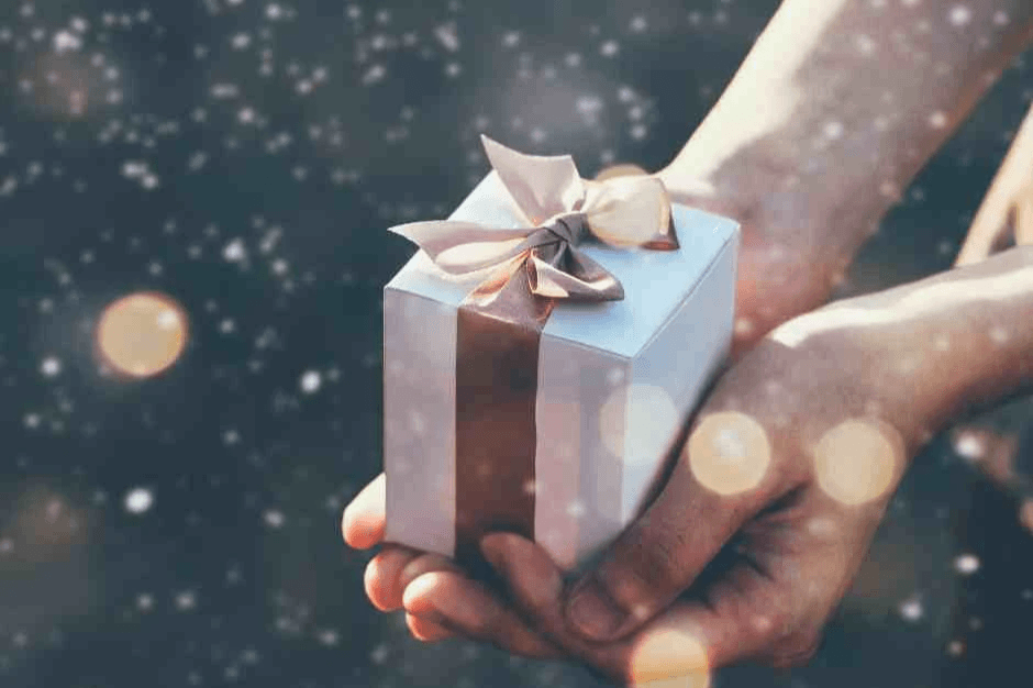 日初而皂手工皂節慶禮盒，雙手捧著綁有緞帶的白色禮物盒，背景帶有溫暖光點