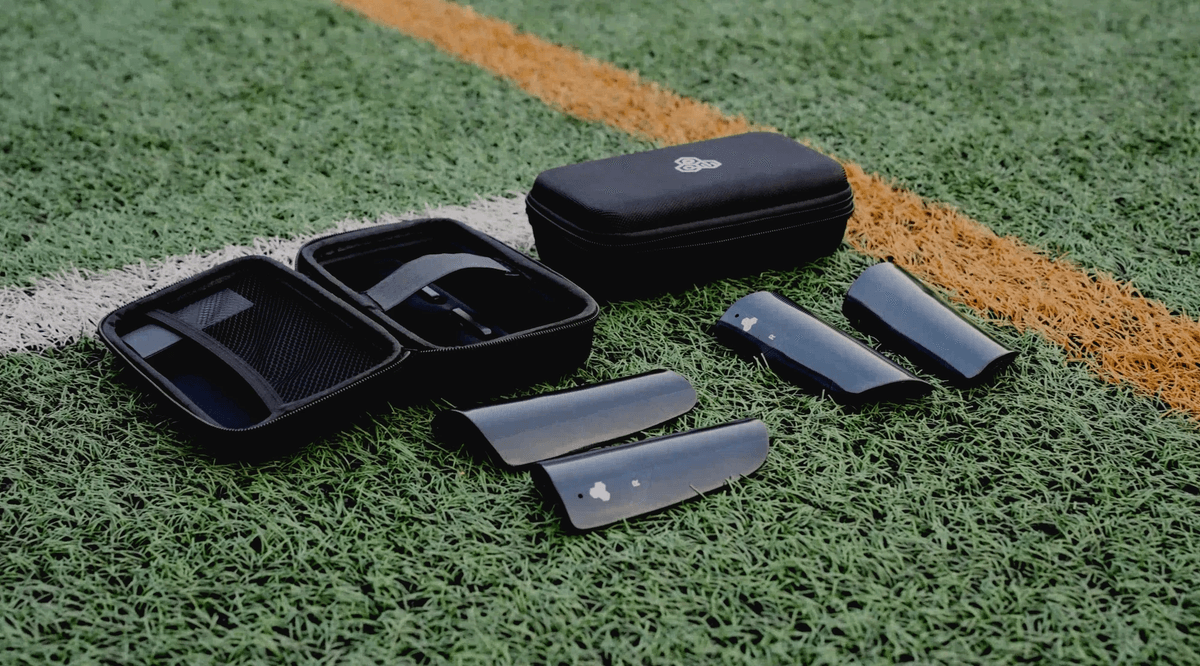Two sets of INSAIT JOY smart shin guards placed on a football pitch, representing the next generation of football player trackers.