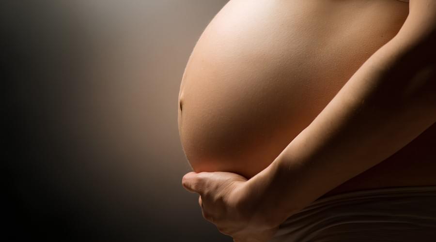 Vientre redondeado de una mujer embarazada sostenido por su mano, luz suave, masaje premamá en Labenne