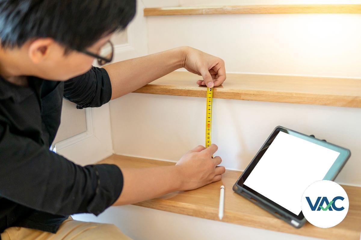 A male access consultant is measuring the height, or riser, or a stairway and is using a tape measure, while looking at a tablet PC screen (2)