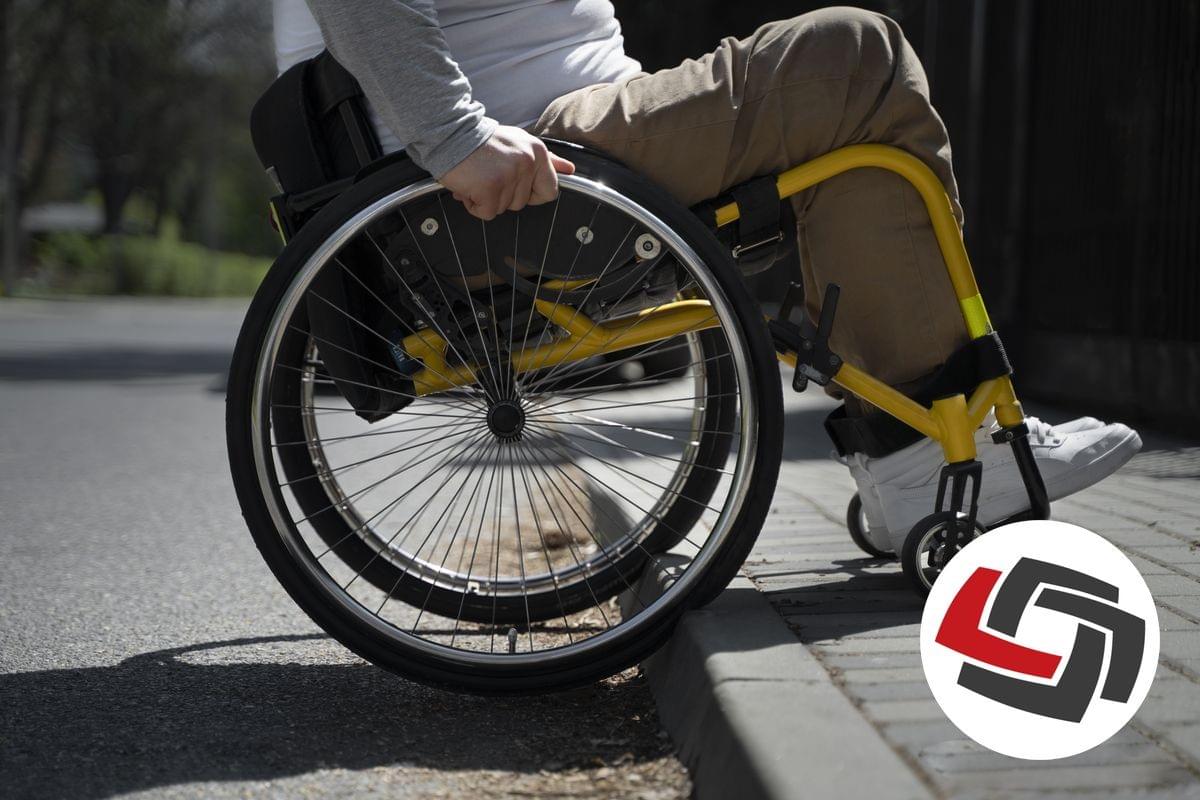 A wheelchair user is attempting to move over a kerb at the junction of a road surface to a raised footpath