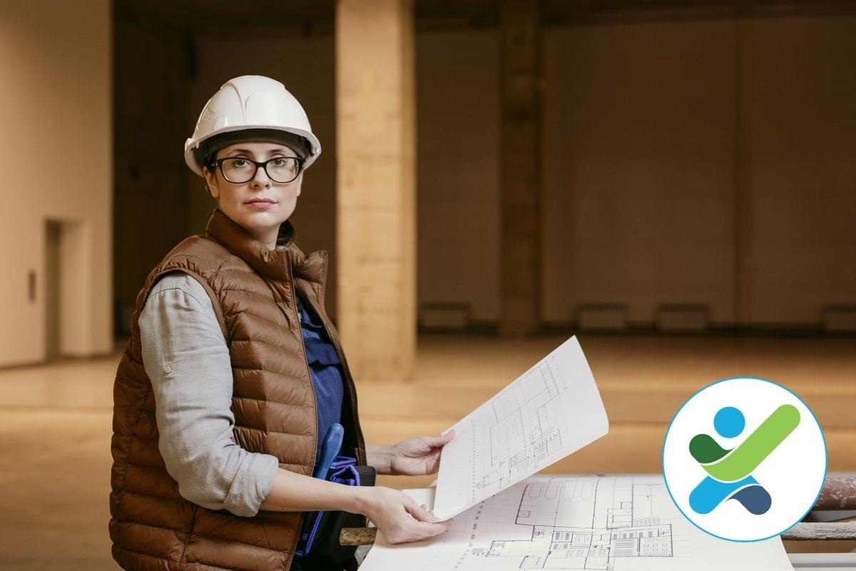 A female access consultant wearing a hardhat is staring at the camera while holding an architectural drawing