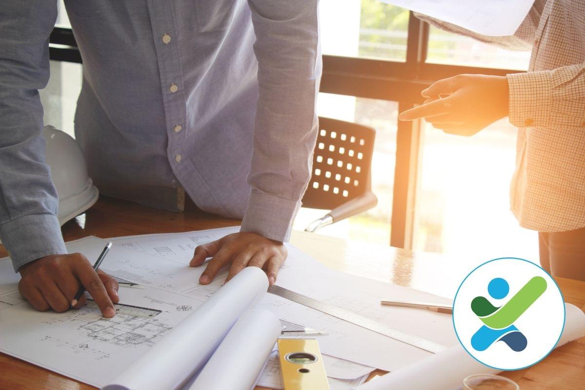 Two access consultants are standing at a desk with architectural drawings on it, one is holding a pencil and pointing at an issue