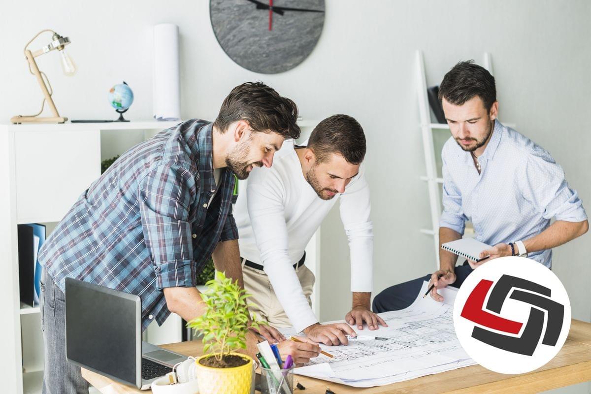 Three men are looking at an architectural drawing on a desk and pointing at an issue