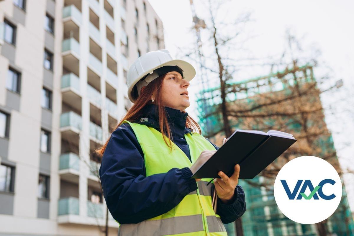 Two male access consultants are standing outside and wearing hardhats while looking at an architectural drawing, one is pointing at the construction site
