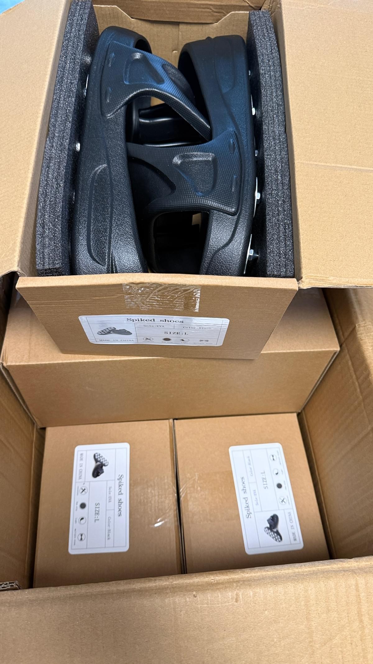 Black spike shoes packed in a shipping box with size label and protective foam for epoxy floor coating work.