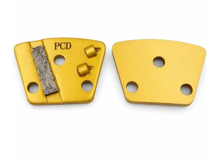 Front and back views of a gold 3-hole trapezoid PCD coating removal tool with stabilizer features