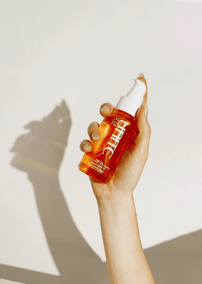 Hand holding a Unite U Oil treatment bottle against a white background, with sunlight casting a dramatic shadow. Hand holding a Unite U Oil treatment bottle against a white background, with sunlight casting a dramatic shadow.