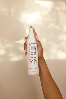 Hand holding Unite Boosta Volumizing Spray against a softly lit backdrop with natural shadow patterns, highlighting the styling product. Hand holding Unite Boosta Volumizing Spray against a softly lit backdrop with natural shadow patterns, highlighting the styling product.