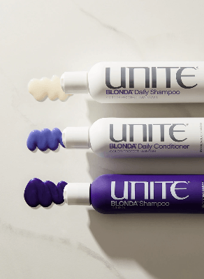 Three Unite Blonda haircare bottles — shampoo, conditioner, and toning shampoo — arranged horizontally with creamy product swirls beside caps. Three Unite Blonda haircare bottles — shampoo, conditioner, and toning shampoo — arranged horizontally with creamy product swirls beside caps.