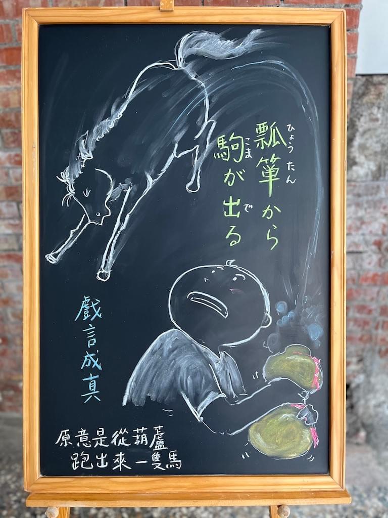 小さい黒板にチョークで絵が描いてあります。日本語のことわざ・慣用表現を紹介するための絵です。右下に男の子が瓢箪を両手で持っていて、そこから馬が飛び出て来たイラストです。馬は右下から左上に大きく飛び上がっています。男の子はびっくりして左上を見上げ、馬は目をつぶって怖がっているようです。