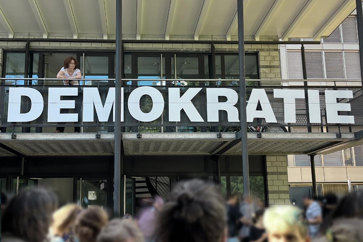 An der Balustrade eines Gebäudes steht in grossen Buchstaben “Demokratie”