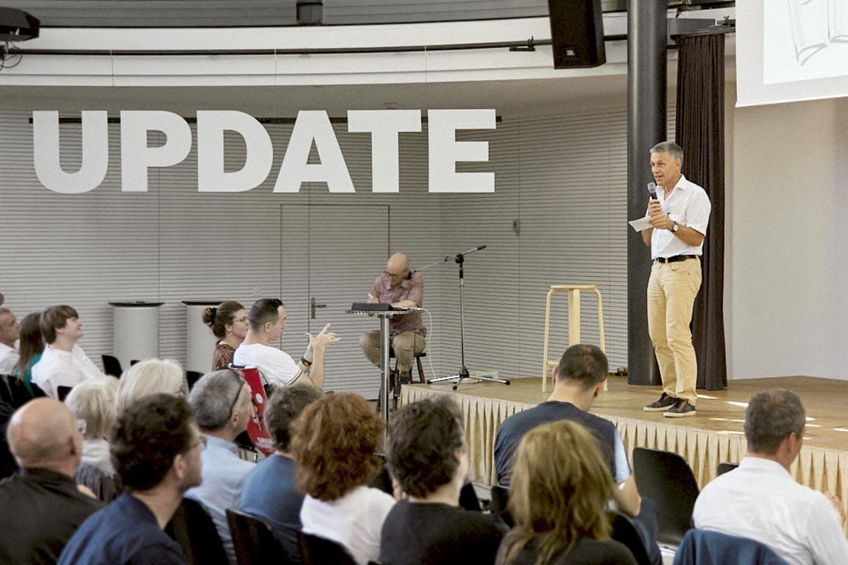 Eine Person spricht von der Bühne aus zu einem vollen Saal