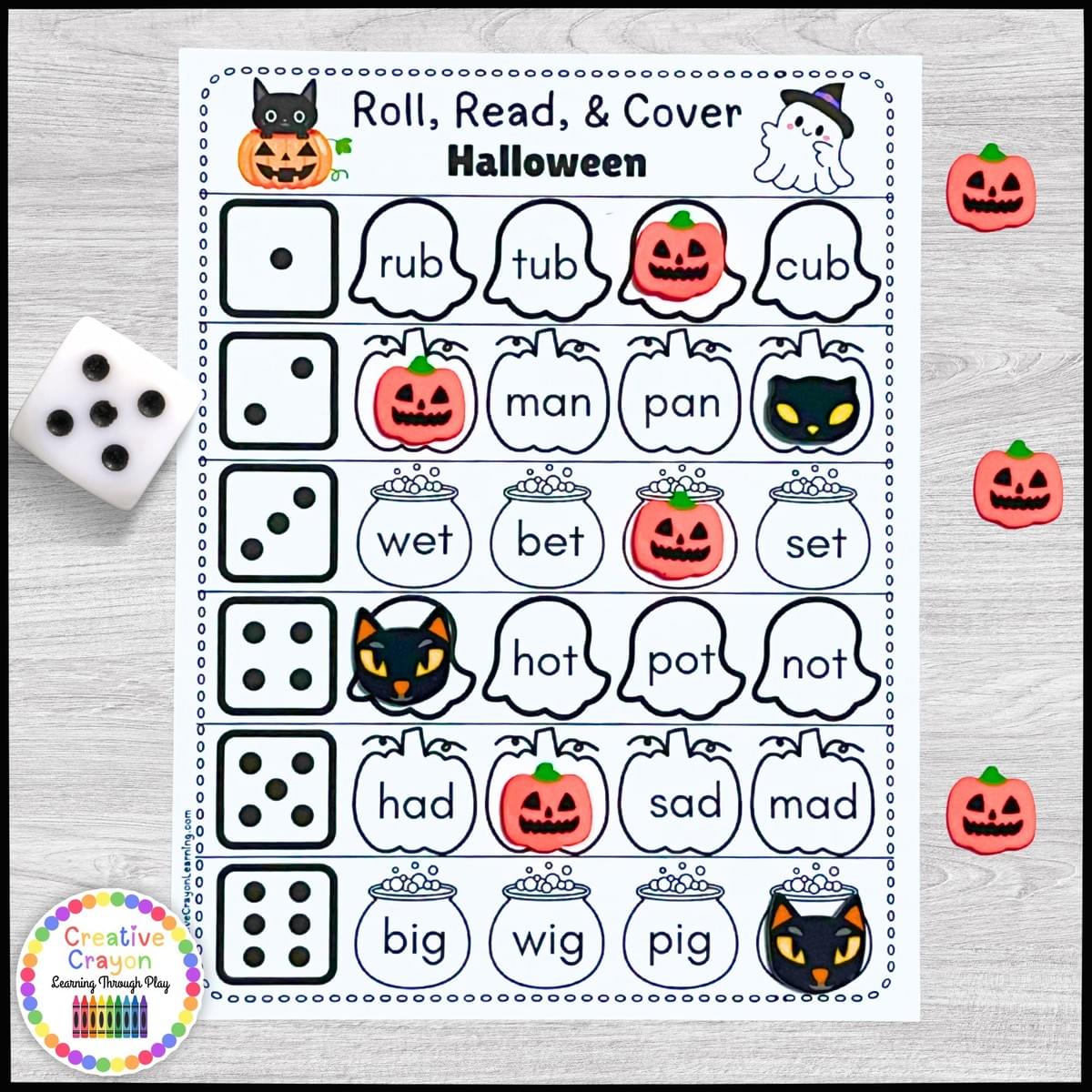 Halloween CVC word roll-and-cover literacy game for kindergarten with dice, word cards, and bingo chips.