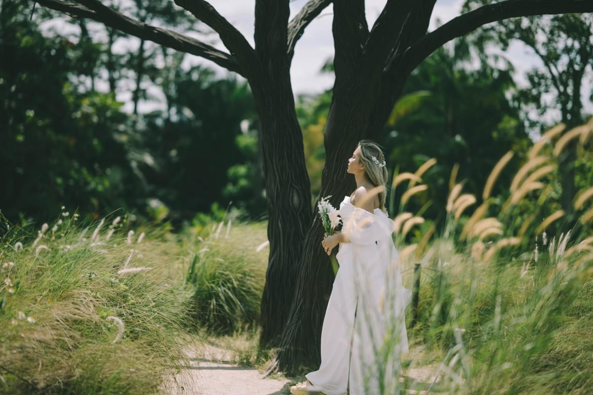 Bride in white gown with bouquet, standing among tall grass and trees at Lakeside Park