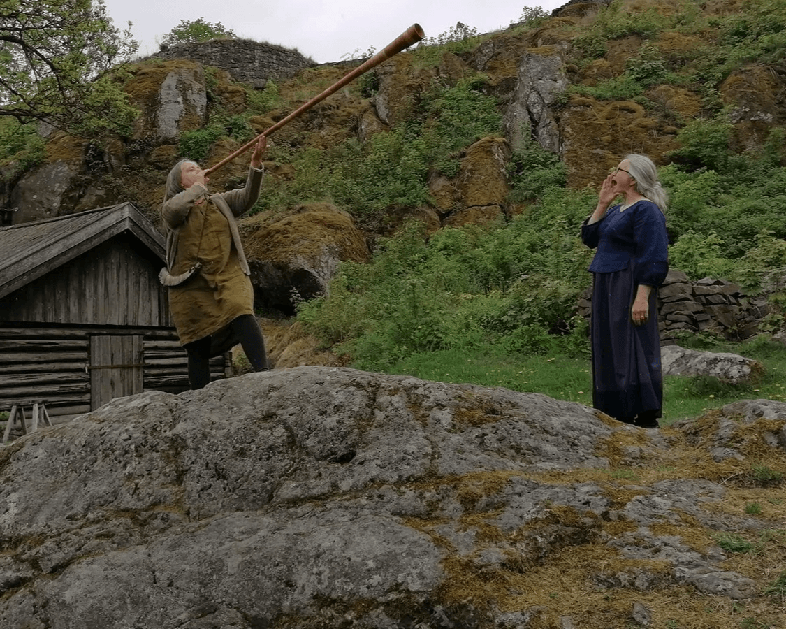 Lurblåsing og lokking framom lafta hus. Foto: Kirsti Holmquist Arntzen