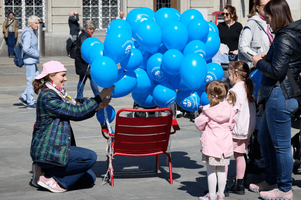 Deux filles attendent qu'une femme leur donne l'un des nombreux ballons bleus de l'initiative pour un congé familial mis à disposition.