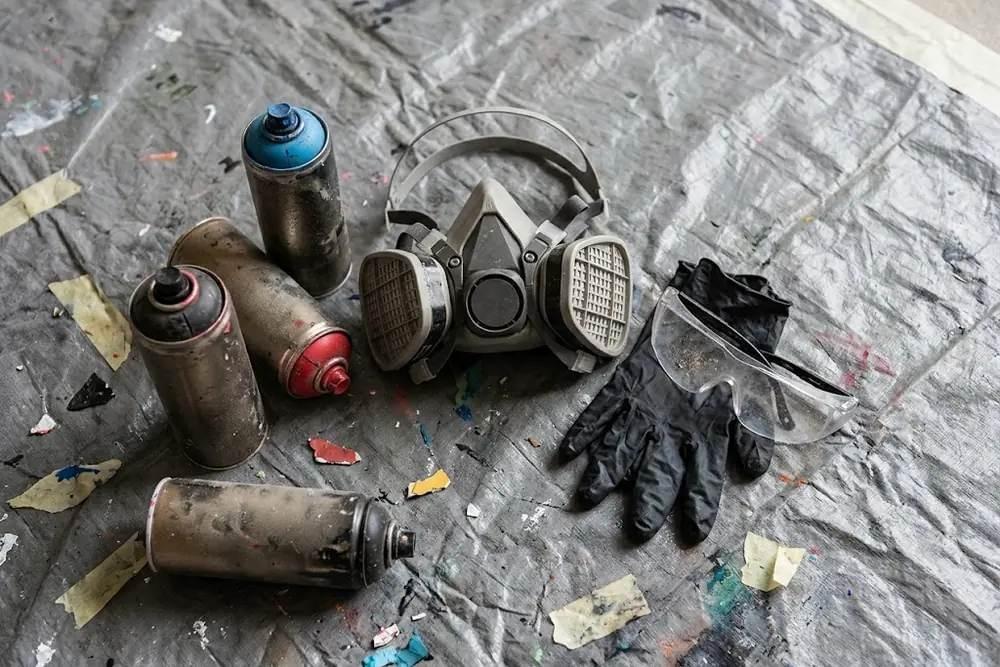 Masque à cartouches, gants nitrile et lunettes posés à côté de bombes aérosol