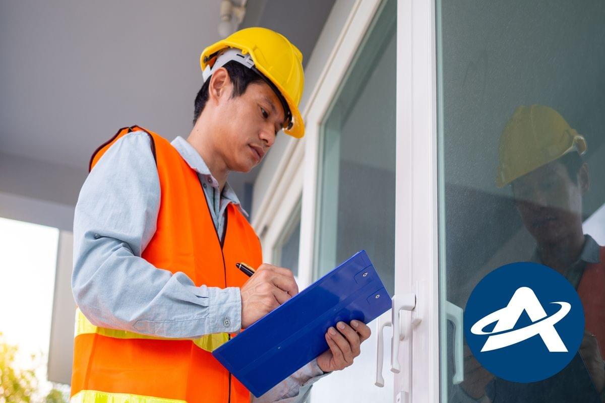 A male access consultant in a hardhat and high visibility vest is checking a doorway and taking notes