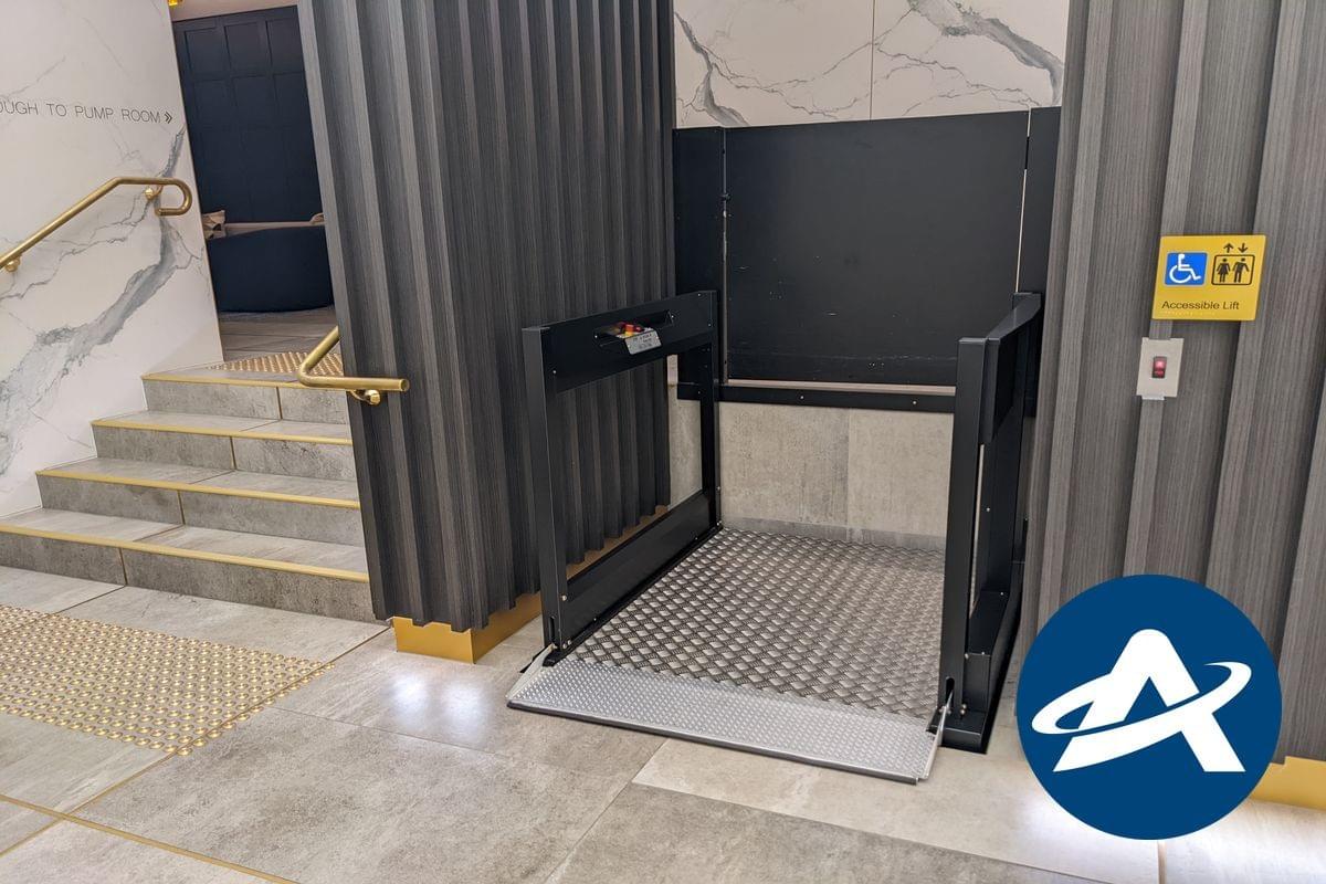 A modern low-rise platform lift is located next to a stairway at the entrance to a building