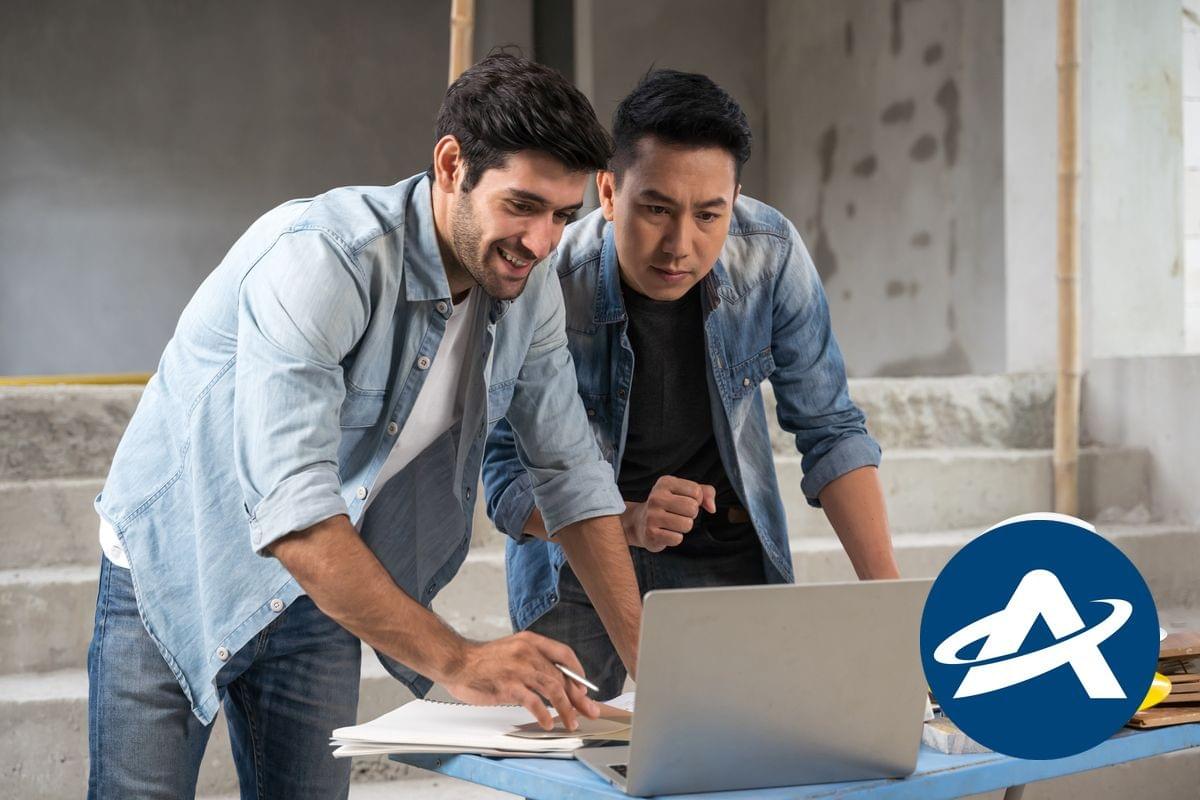 Two men are looking at a laptop on a desk and one is smiling