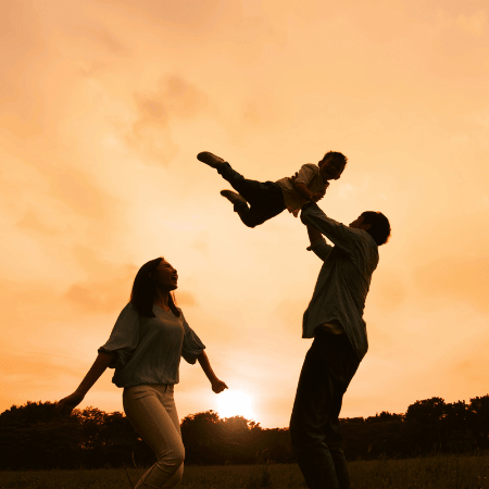 Father lifting child playfully into the air as mother watches, all sharing a joyful family moment.