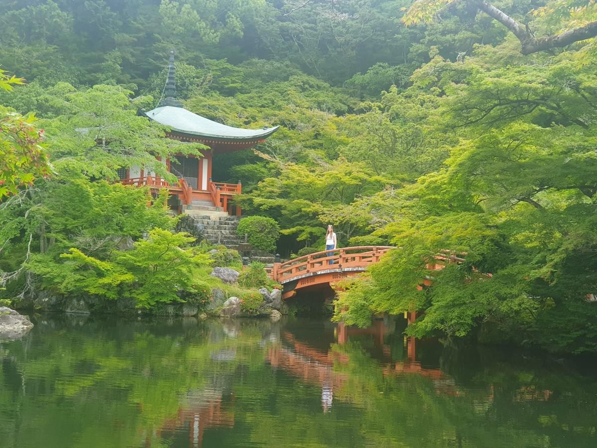 Kyoto's quiet temples, standing on a red bridge at Daigo-ji temple in Japan, surrounded by trees and reflected in still water