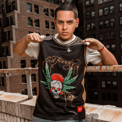 Man on a rooftop wearing a black and gold Ed Hardy basketball jersey with a rhinestone skull graphic.