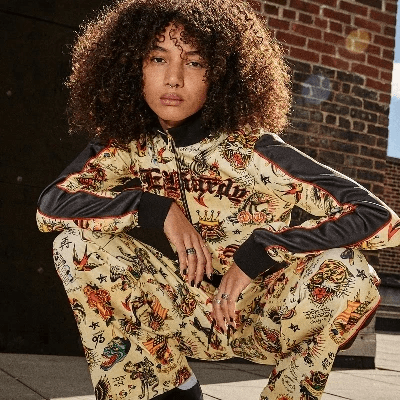 Person wearing a matching tattoo-print track jacket and pants set with colorful Ed Hardy-inspired graphics.